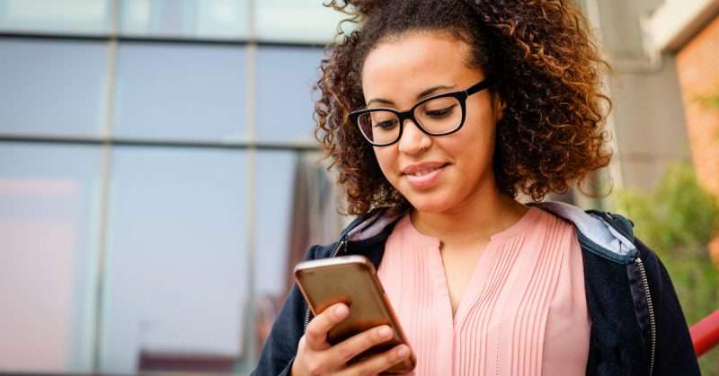 a young woman in a pink shirt and glasses looks at a mobile phone