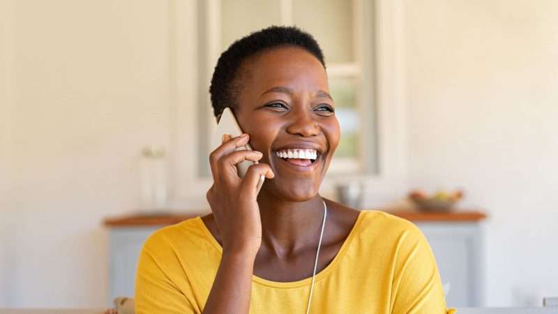 smiling woman in yellow shirt using a telephone 