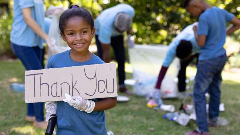 smiling girl in blue holds a thank you sign