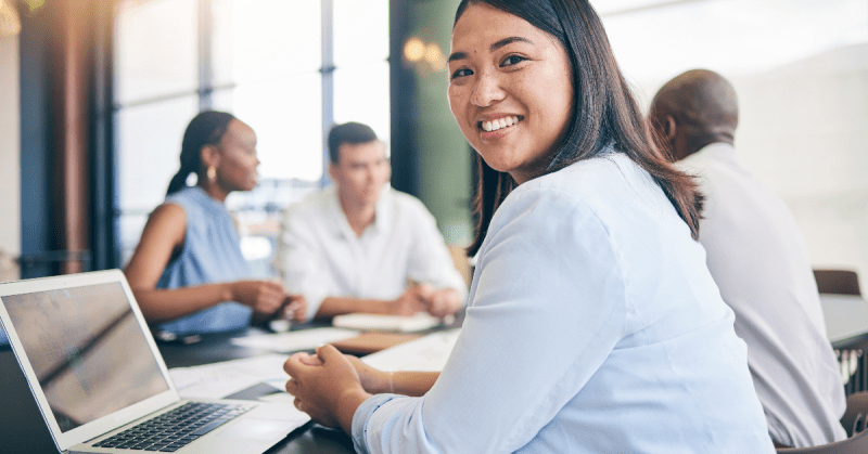 A woman smiles at the viewer in an office meeting